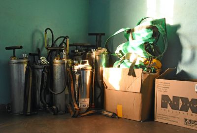 IRS spraying equipment in the corner of a green room with a brown floor and a box with equipment to the right of the image.