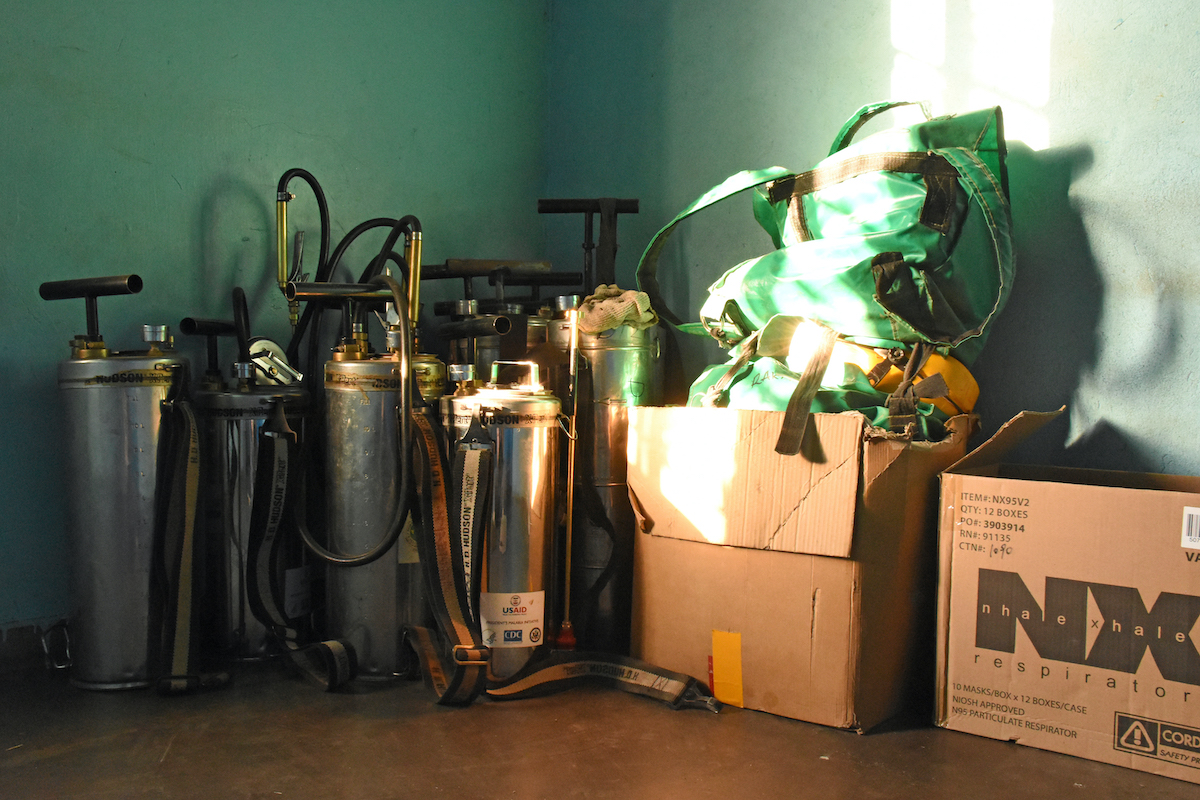 IRS spraying equipment in the corner of a green room with a brown floor and a box with equipment to the right of the image.