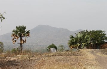 Ugandan landscape showing a dirt road, trees, house and mountain in the distance