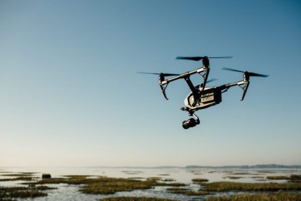 Image of an estuary with a grey and black drone hovering above the right side of the image with a blue sky in the background