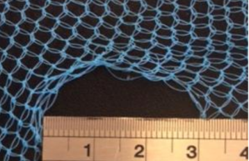 Image of blue netting against a black background with a hole in the bottom centre of the net fabric. A silver ruler at the bottom of the image is laid across the diameter of the hole, showing the hole is 3 cm wide.