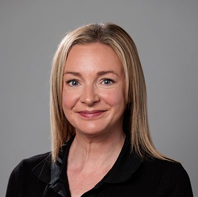 Image of a woman with straight, blonde hair and blue-grey eyes wearing a black blouse.