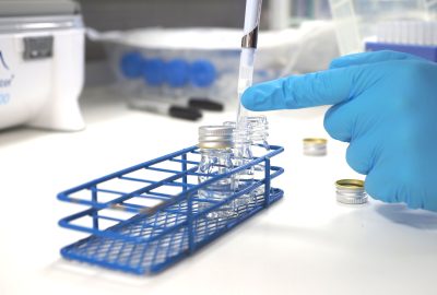 Hand in blue latex glove pipetting into clear tubes in a blue tube rack