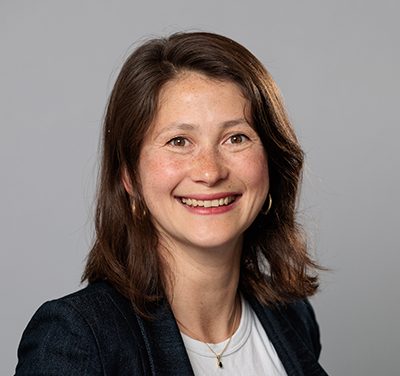 Image of a smiling woman with short brown hair and brown eyes wearing a black blazer and a white t shirt